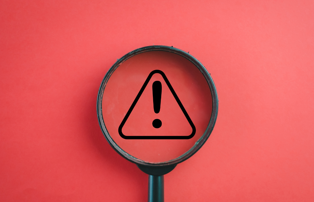 A magnifying glass highlighting a triangular caution symbol with an exclamation mark on a red background.